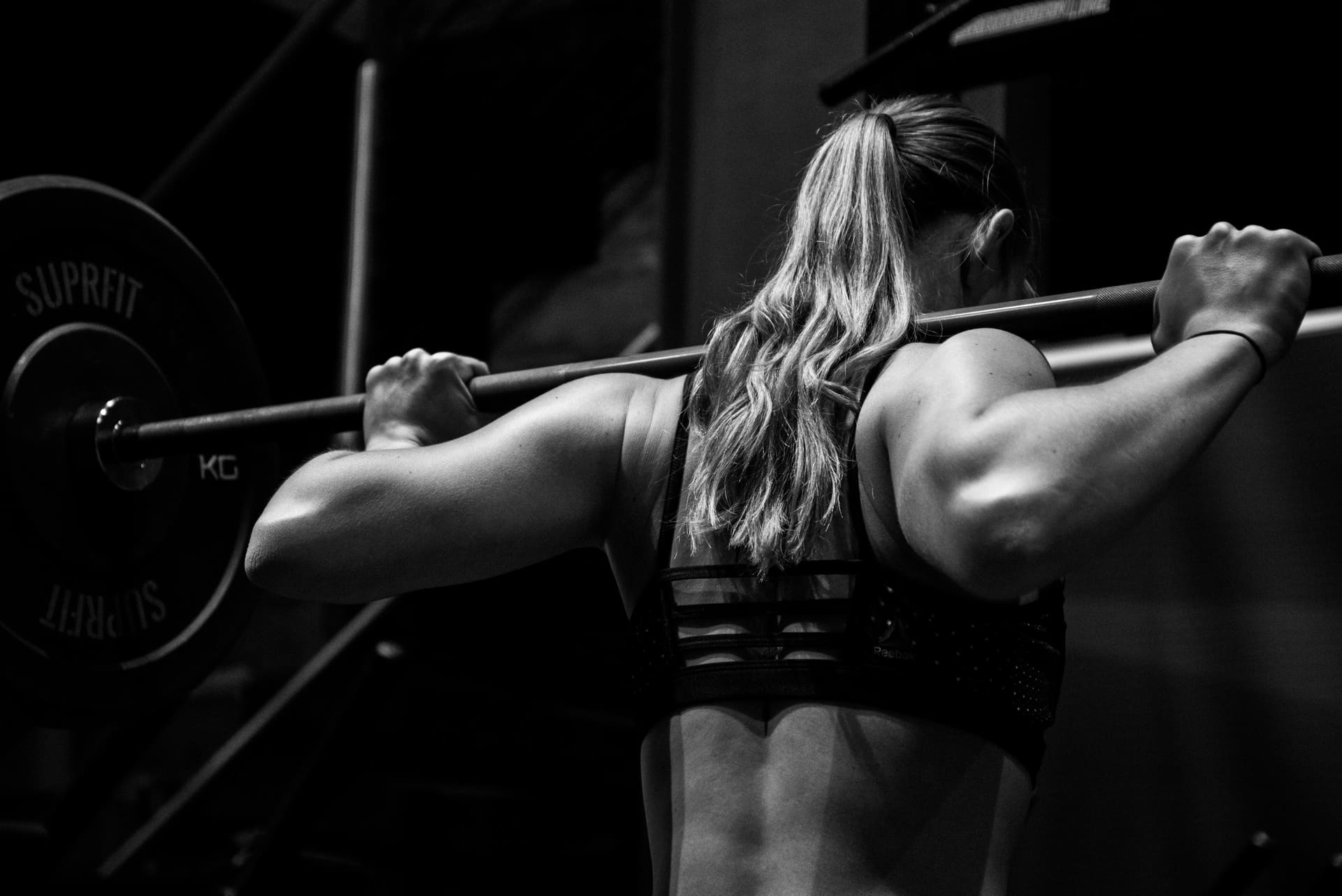 A woman racking a barbell on her shoulders mid-squat, back muscles engaged, in the SomaStrong home studio